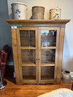 Front view of the rustic pine display hutch showing two glass paneled doors and three ceramic crocks on top.