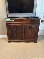 Front view of wooden storage/buffet cabinet with TV on top, showing two paneled doors and two drawers with metal knobs.