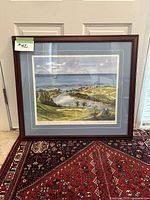 Framed print leaning against door showing golf course art with mat and dark wood frame.
