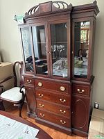 Front-left angle view of the vintage mahogany china cabinet showing glass doors, drawers, brass handles, and detailed woodwork.