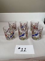Front view of 6 hand painted bird glass tumblers arranged in two rows. Colorful bird and leaf designs visible.