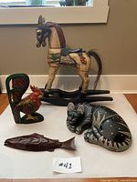 All four carved wooden items displayed on white paper: rocking horse, curled cat, standing rooster, carved fish panel.
