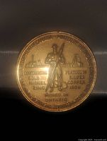 Close-up front view of 1967 Canadian mining medallion in bronze tone metal, featuring miner figure, mining equipment background, and metal composition text around edge.