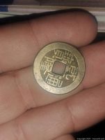 Front side of the bronze coin with Chinese characters and square center hole, held in hand for scale.