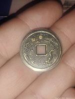 Obverse of coin showing raised dragon design with intricate detailing encircling a square hole.