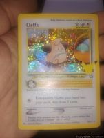 Close-up photo of a Cleffa holographic foil Pokémon card held in hand showing detailed text, HP, and illustration.