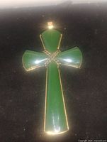 Photo of green faux jade cross pendant on black background showing shape, color, and gold-tone metal trim detail.
