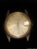 Close-up of Gruen men's gold tone quartz wristwatch face showing gold dial, date magnifier, and textured bezel.