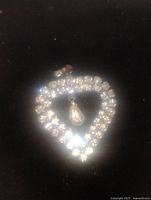 Heart-shaped pendant made of clear rhinestones with a dangling pear-shaped rhinestone in center, metallic loop for chain attachment visible.