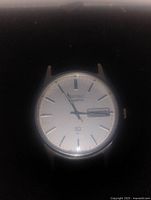 Close-up photo of Seiko men's watch face showing silver dial with stick indices and day-date window.