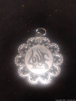 Front view of round sterling silver pendant with delicate lace-like border and decorative center design.