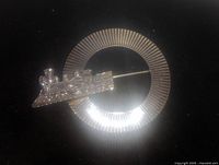 Close-up photo of vintage train brooch showing detailed steam locomotive design in silver-tone metal on circular textured backing, with pin closure visible.