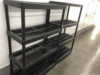 Two black plastic shelving units, each with three slatted shelves and standing side by side.
