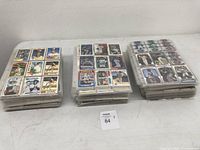 Three large stacks of baseball cards in clear 9-count protective sleeves, each stack containing many cards arranged neatly.
