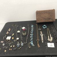 Jewelry assortment on black cloth showing multiple necklaces, bracelets, earrings, and a carved wooden box