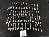 Top-down image showing all 48 miniature collectible souvenir spoons arranged on a black surface to display various designs including crests, shields, and landmarks.