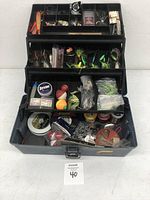 Open fishing tackle box showing multiple trays with assorted fishing lures, lines, floats, and tools.