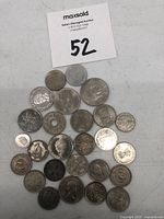 Top view of 25 assorted foreign coins, various sizes and with different designs including portraits, symbols, and inscriptions