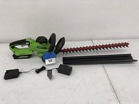 Greenworks cordless hedge trimmer laid out with blade cover, battery attached, and charger.