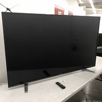 Full view of LG 65 inch flatscreen TV with remote placed in front, showing the TV turned off.