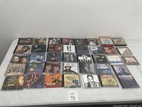 Top-down view of 32 various artist CDs arranged on a grey table showing different cover artworks and artist photos.