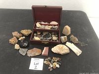 Overall view of assorted stones and minerals displayed on a table with a small wooden box, showing a wide variety of shapes, colors, and sizes.