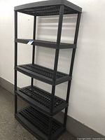 Full view of black plastic 5-tier shelving against white wall showing shelf perforation.