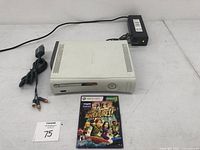 White Xbox 360 console with power supply cable and Kinect Adventures game disc on a white surface.