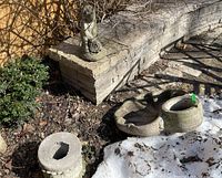 Photo of the concrete birdbath basin, base, and lawn figure outdoors with fallen leaves and some snow around, showing general wear and natural weathering.