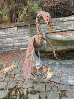 Front-side view of metal bird sculpture showing the long neck, textured feathers, and extended wings on a stone patio.