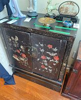 Front view of wood cabinet showing floral and bird motifs, metal latch, and decorative edge patterns.