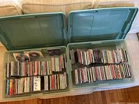 Two open green plastic storage bins filled with CDs in jewel cases showing neatly arranged rows.