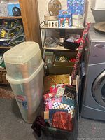 Overall view of plastic bins, wrapping paper rolls, gift bags, boxes, bows on shelves next to laundry appliances