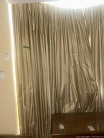 Photo of two beige heavy lined curtain panels hanging with light shining through gaps and subtle texture visible.