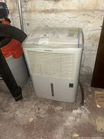 Front view of white Simplicity SDR307EE dehumidifier with water level indicator and control switch, placed in basement setting.