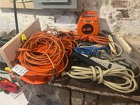 Full lot view showing assorted extension cords, power bars, and a cord caddy on a table against a basement wall.