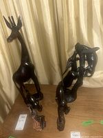 Photo showing four carved African ebony wood figurines including a tall giraffe and a monkey figure on a tree trunk with broken tail.