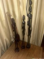 Three handcrafted African ebony wood figurines displayed against a curtain background, showcasing their height and carving details.
