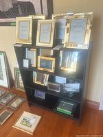 Wide view of black shelving unit filled with assorted glass and metal picture frames in silver, gold, and mirrored finishes