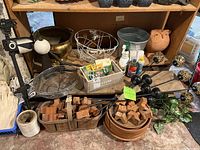 General overview of garden tools, terra cotta planters, lamp stakes, fertilizers and gardening gloves in basket and shelf.