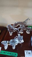 Photo of five clear glass animal figurines by Kosta Boda displayed on wooden surface, including lion, cat, dog, horse, and pig.