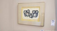 Framed wall art hanging on a wall, showing four stylized owls with big eyes and geometric patterns, framed with beige and yellow mats in a light wooden frame.