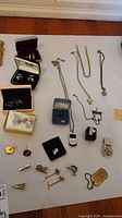 Full view of assorted men's jewelry on white background showing boxes with cufflinks, chain necklaces, tie clips, tie tacks, pin, and money clip.