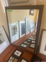 Full view of the large rectangular mirror leaning against a wall, showing frame details and reflections of framed art nearby.