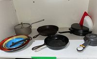 Overview of one shelf with various pans, skillets, pot, and plates.