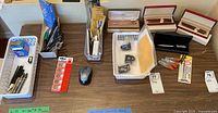 Overview of the lot showing multiple pens, a wireless mouse, pen clips, mechanical leads, and boxed pen sets laid out on a table.