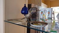 Full view of lot showing blue glass pedestal dish, metal bird figurine, porcelain vase, and decorative plate on a glass surface