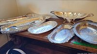 Photo showing multiple silver plated and steel serving dishes on a wooden surface.