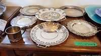 Photo showing multiple vintage silver plated trays and one mug arranged on wooden surface.