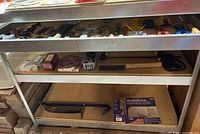 Photo of metal workbench shelves showing wire brush, pry bars, wall repair patch kit, and other tools.